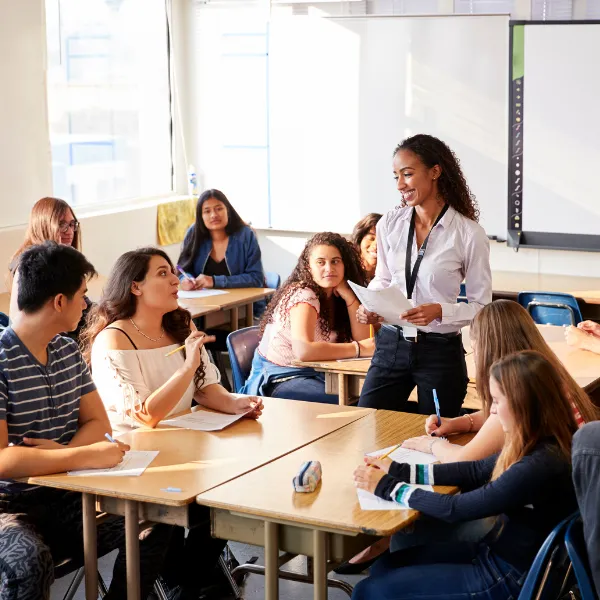 High School Teacher Standing By Student Table Teaching Lesson
