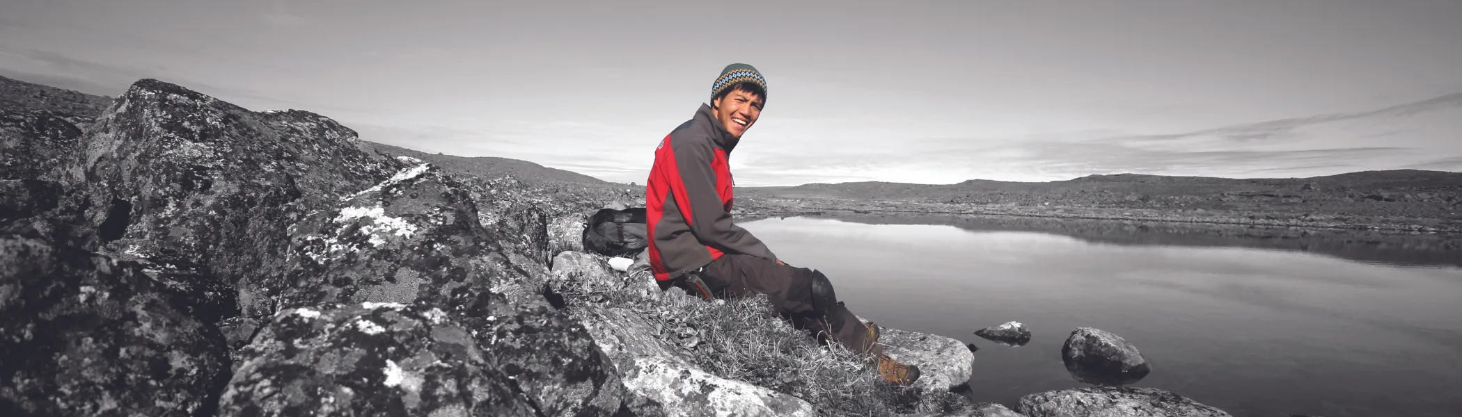 Student sitting on the top of a mountain, smiling at the camera.