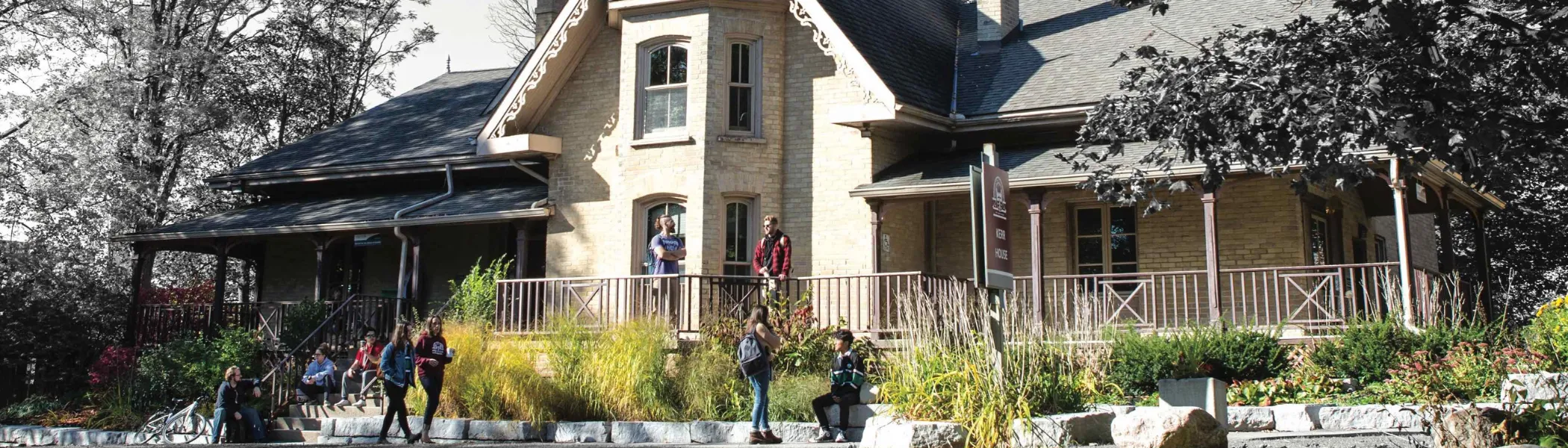 Trent University students standing and talking, outside of Kerr House.