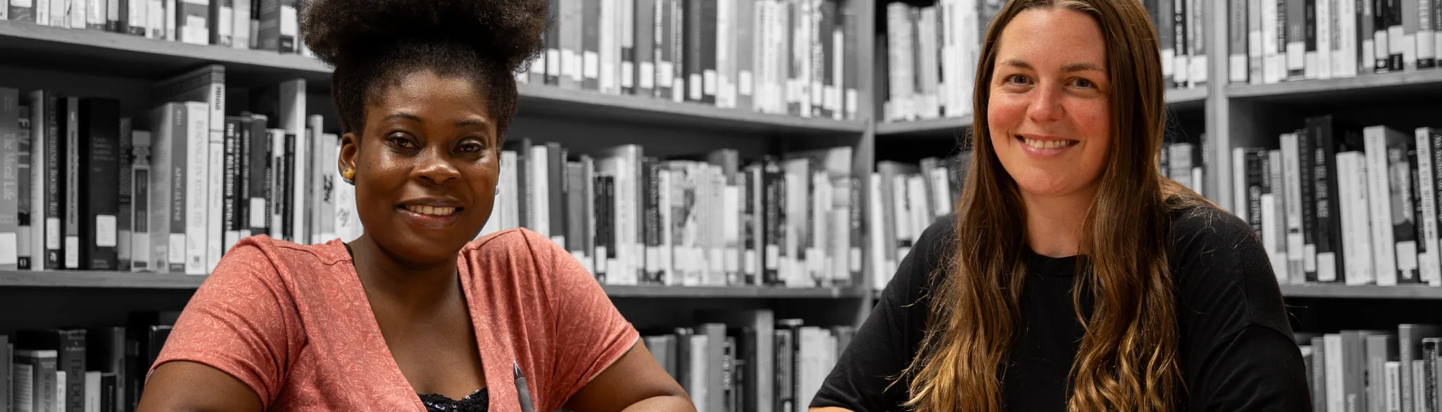 Two Trent University students smiling at the camera, with book shelves in the background.