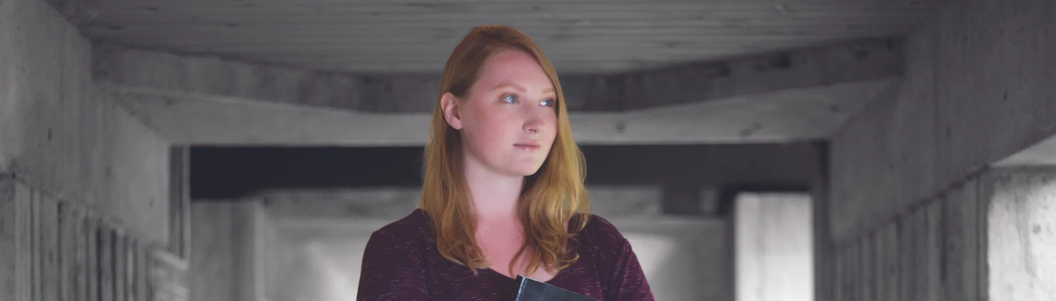 Image of student, standing, looking off in the distances, holding a book.