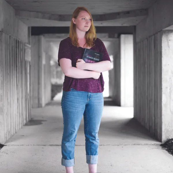 Image of student, standing, looking off in the distances, holding a book.