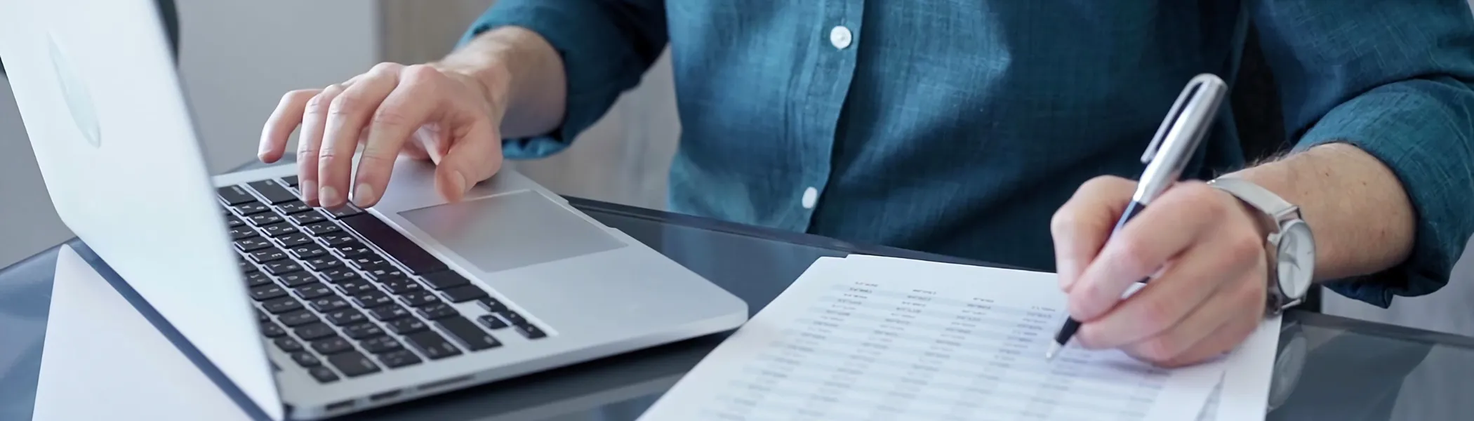 Business person is analyzing data on laptop and paper.