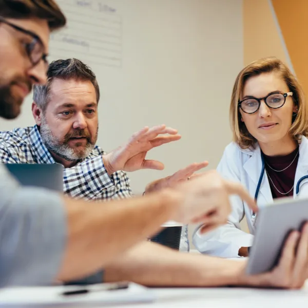 Group of healthcare workers with digital tablet meeting in hospital boardroom.