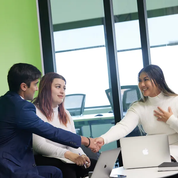 Three Trent University students sitting at a table, with two shaking hands.