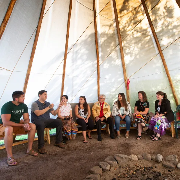 Trent University First Peoples House of Learning students and staff, inside of a tipi, talking.