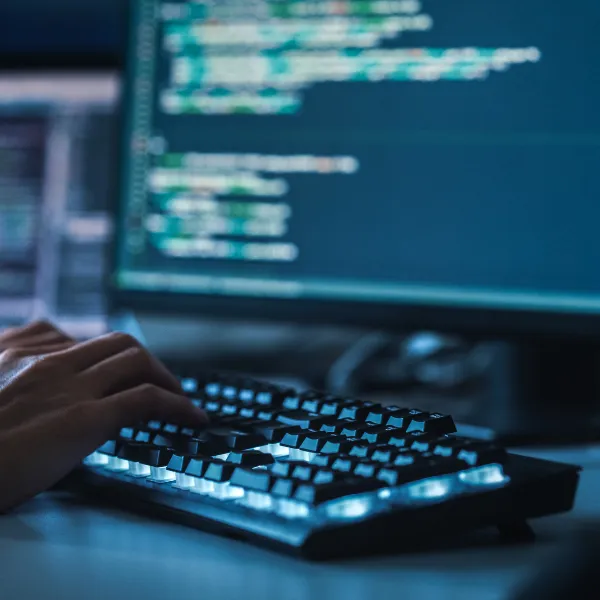 Close-up Focus on Person's Hands Typing on the Desktop Computer Backlit Keyboard. Screens Show Coding Language User Interface.