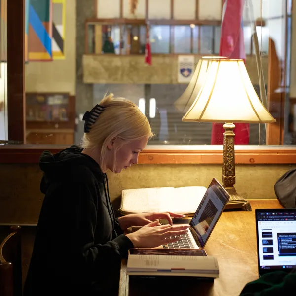 Trent University student working on laptop, with an open book next to them.