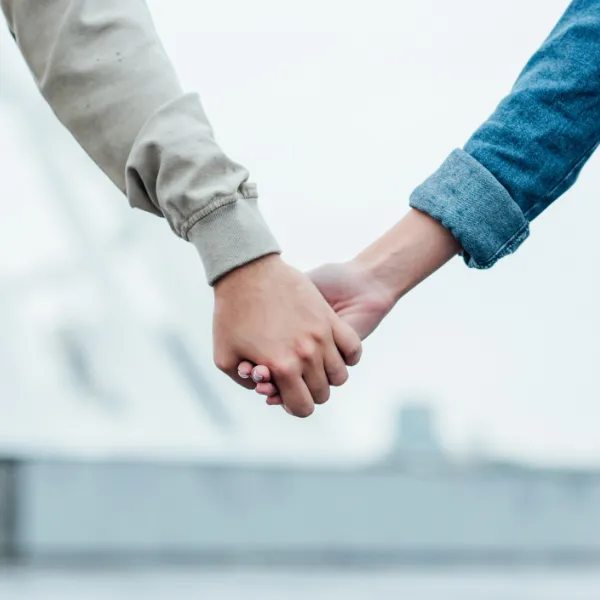 Close-up shot of couple holding hands on street on cloudy day.