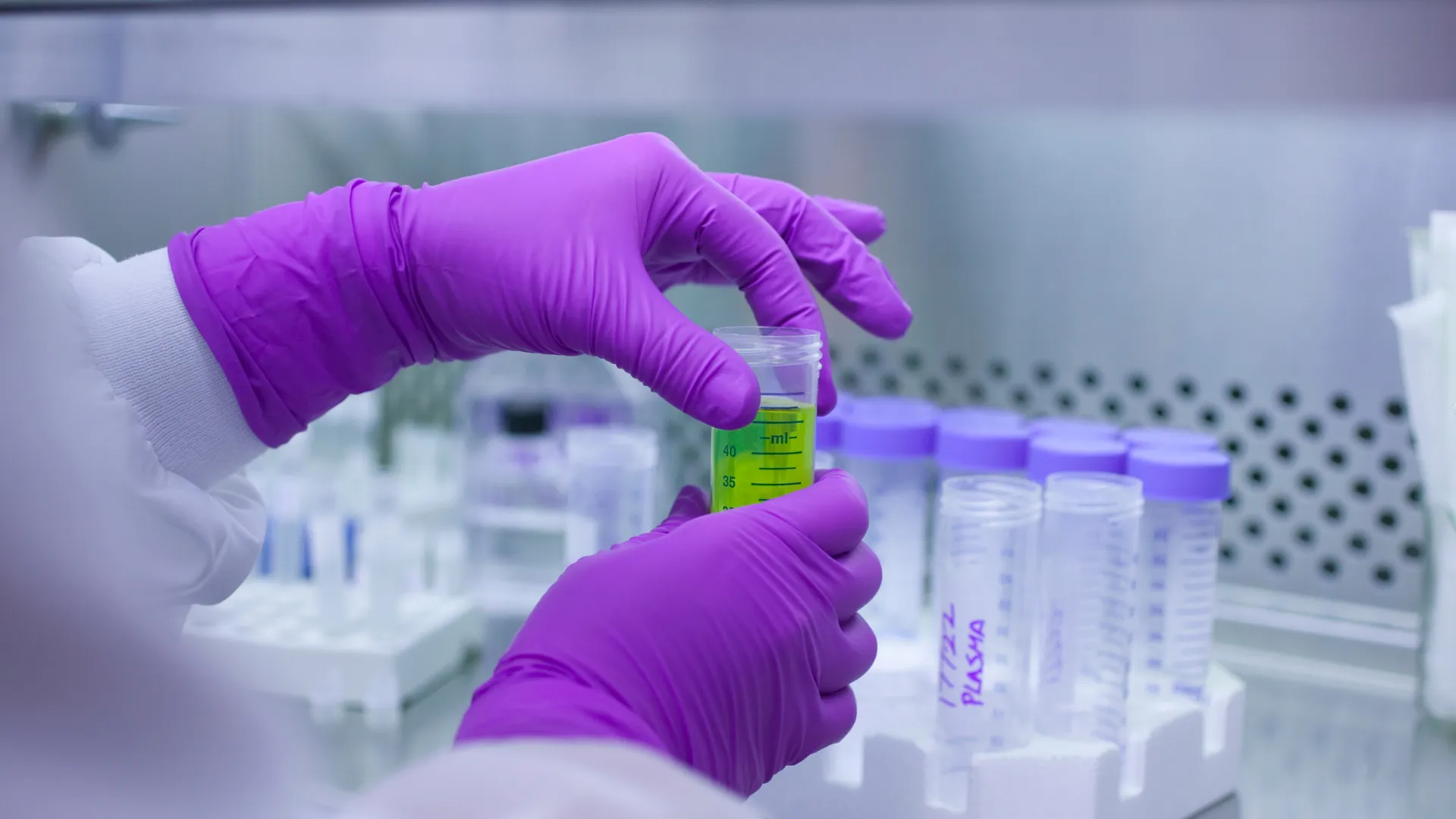 two gloved hands hold a vial of a green solution