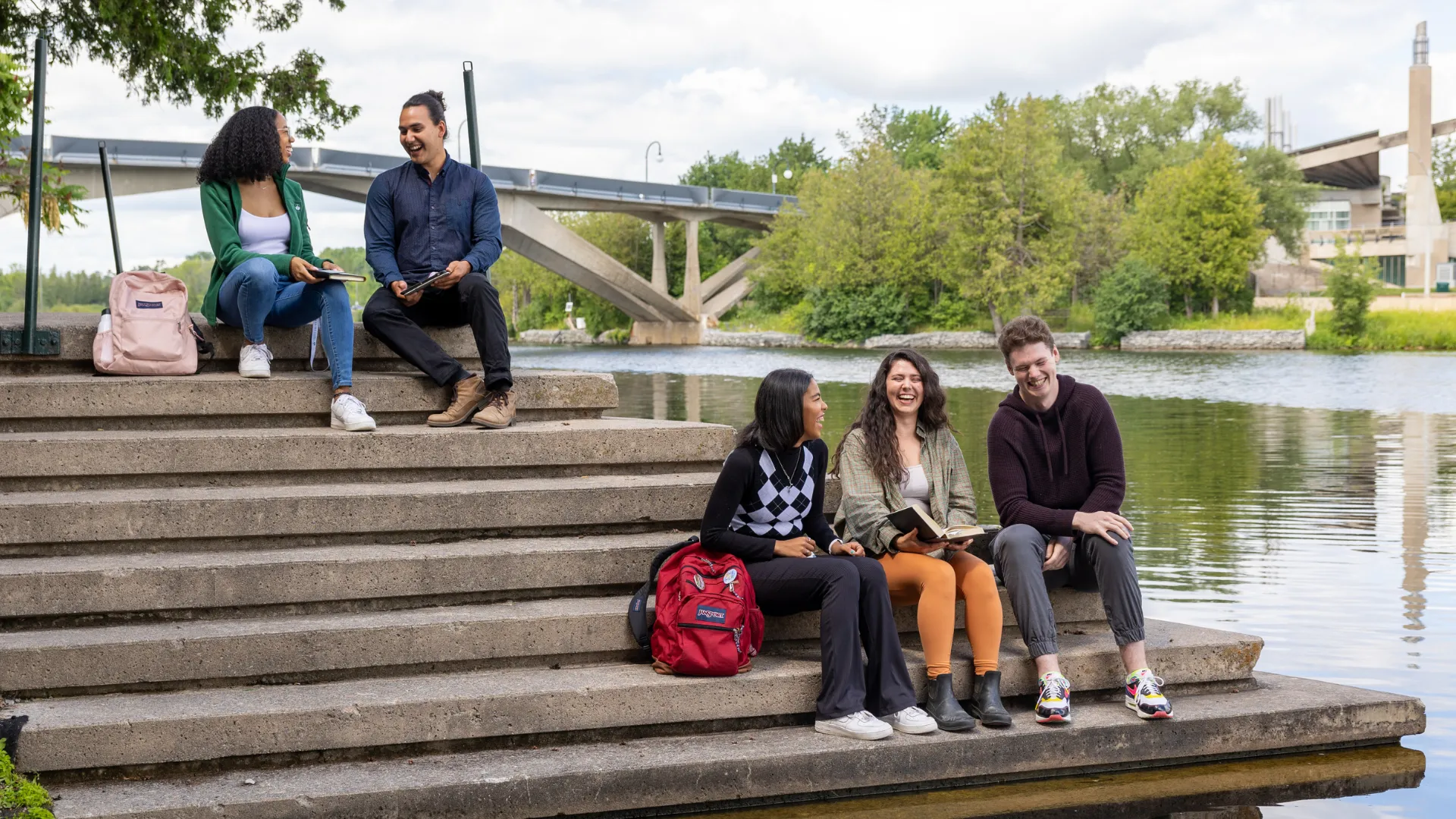 Trent students sitting on the bank of the Otonabee river outside of Bata Library
