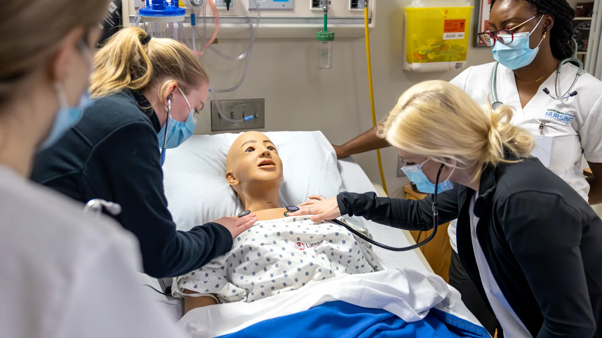 Nursing students practice taking vitals on a training dummy