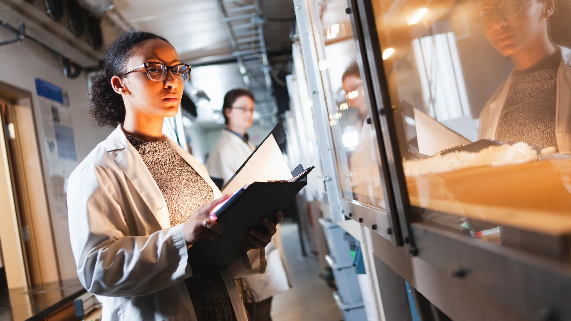 A Trent student in a lab coat writes down readings from a machine