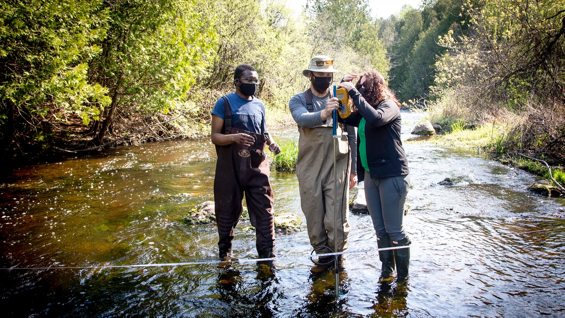 Two students and a professor in a river examining water samples