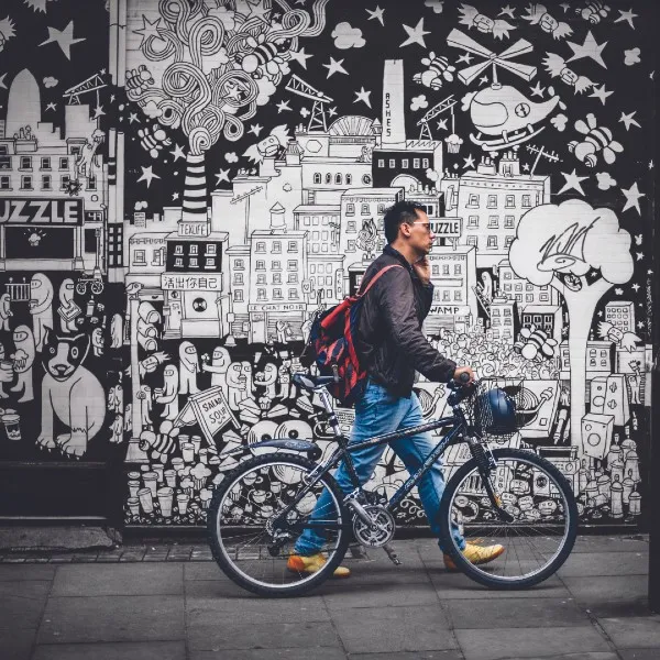 A man walking his bike past a mural