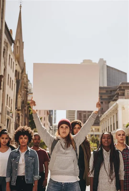 Photo of group of people in a group across a street with a woman in the center holding a blank sign