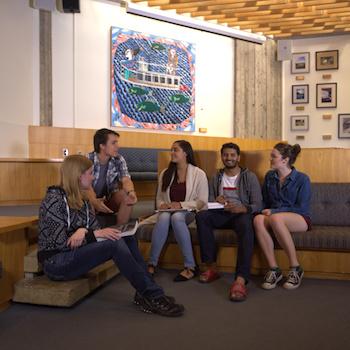 A guy sitting on steps by the river working on his laptop