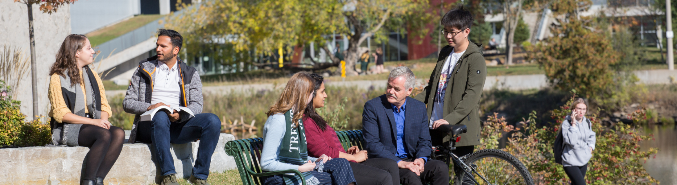 Students sitting on bench talking with Trent University President Leo Groarke
