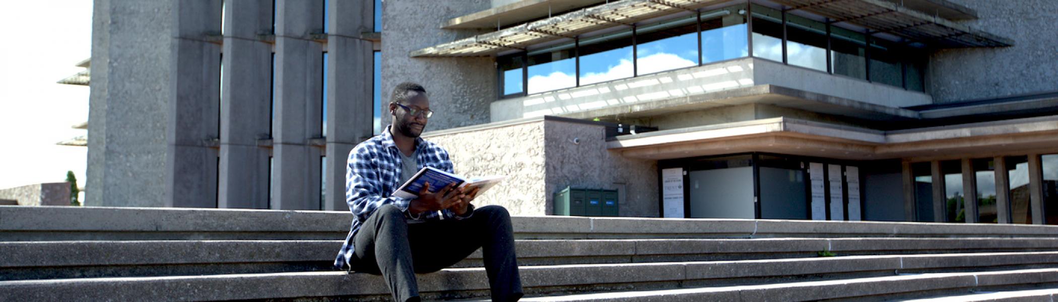 A guy sitting on the steps of Bata Library reading a book