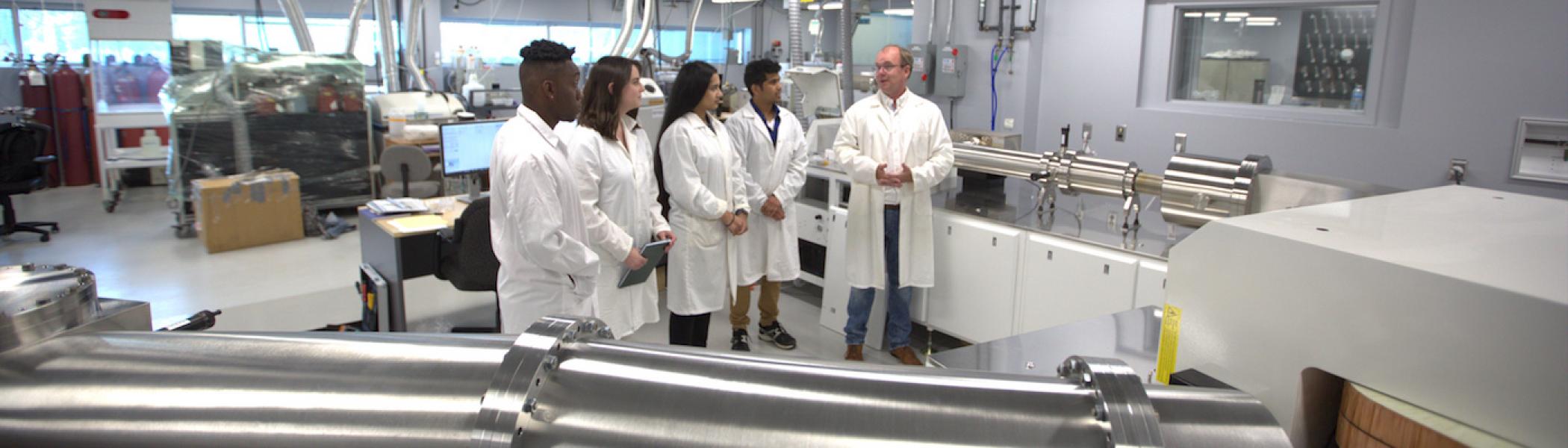 A group of students in lab coats standing with a professor in a lab