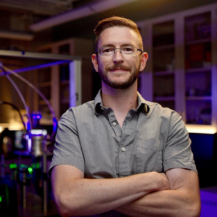 Photo of Ryan Sullivan smiling in a grey polo shirt with arms crossed.