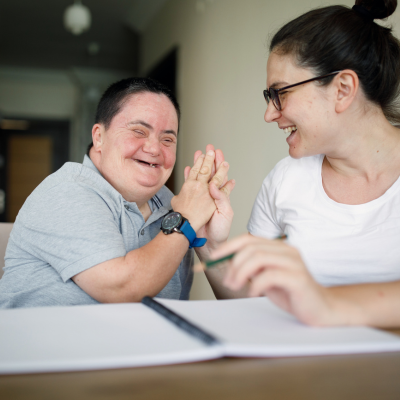 Photo of woman clapping hands with man who has downs syndrome, with a big smile on face