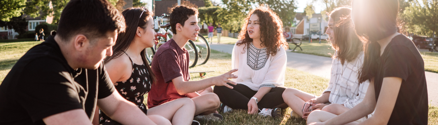 A group of young people sitting in a circle on the ground, talking