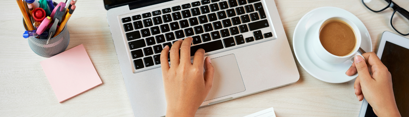 photo of hand on keyboard typing, with cup of coffee beside