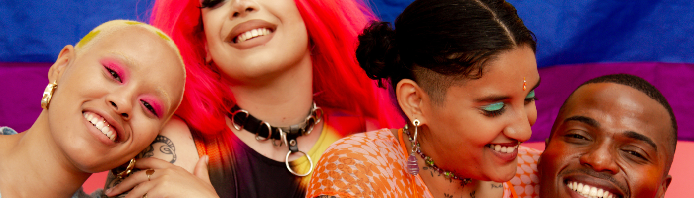 Photo of group of four young people smiling in front of pride flag