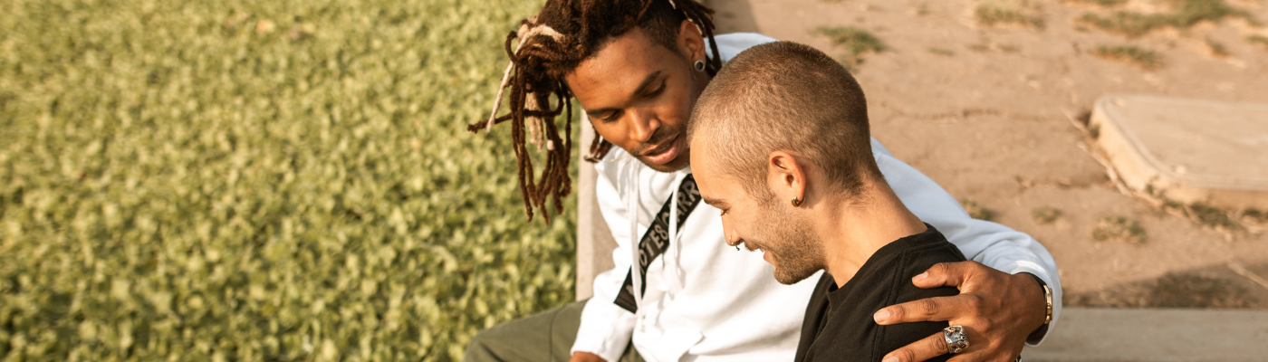 Two men talking, one of colour, with dreadlocks, with arm around another