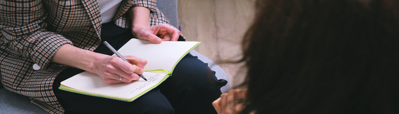 Close-up of woman's hands taking notes in notebook, back of someone's head in forefront of image