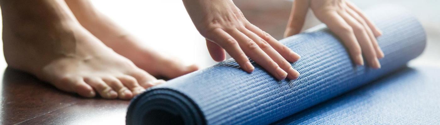 Hands rolling up a blue yoga mat on a wooden floor
