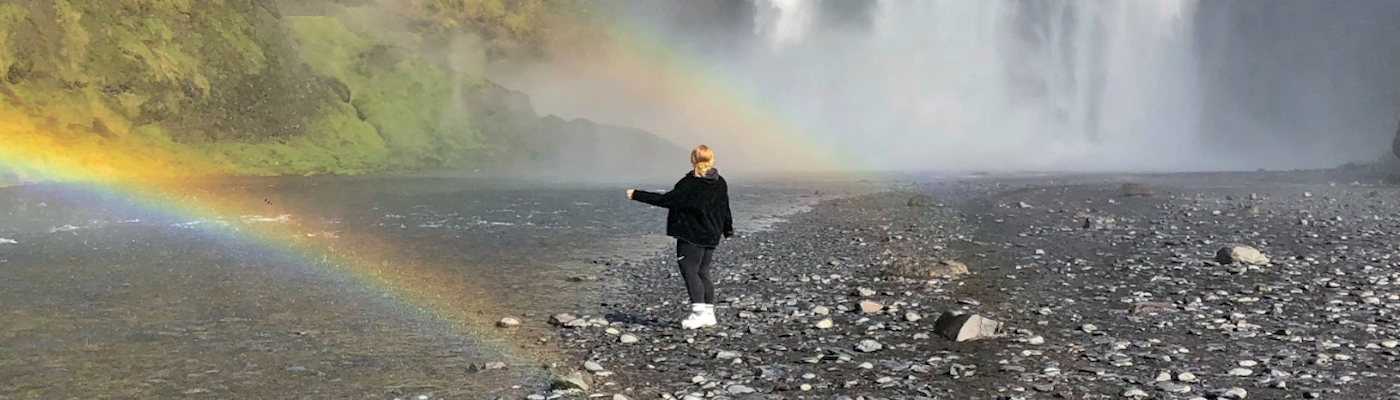 Person standing by a waterfall with two rainbows around them.