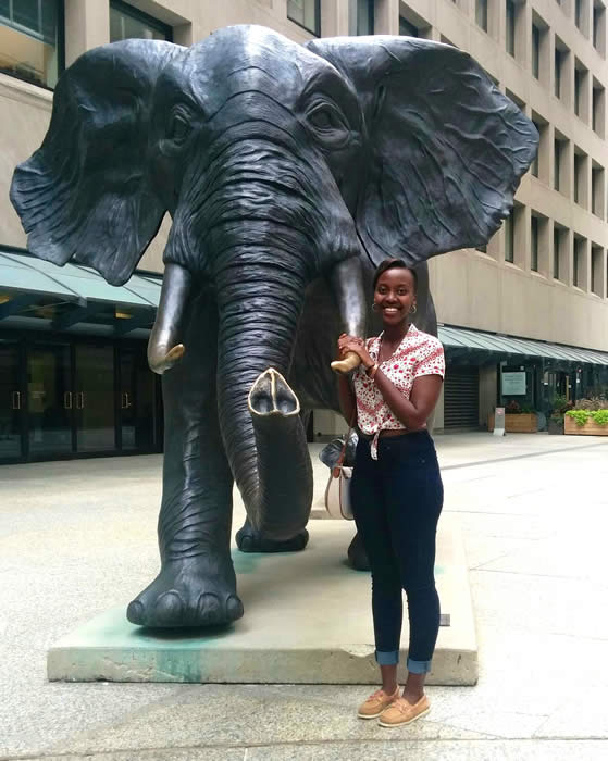 grad student Faith Mwesigye standing beside elephant statue smiling at camera