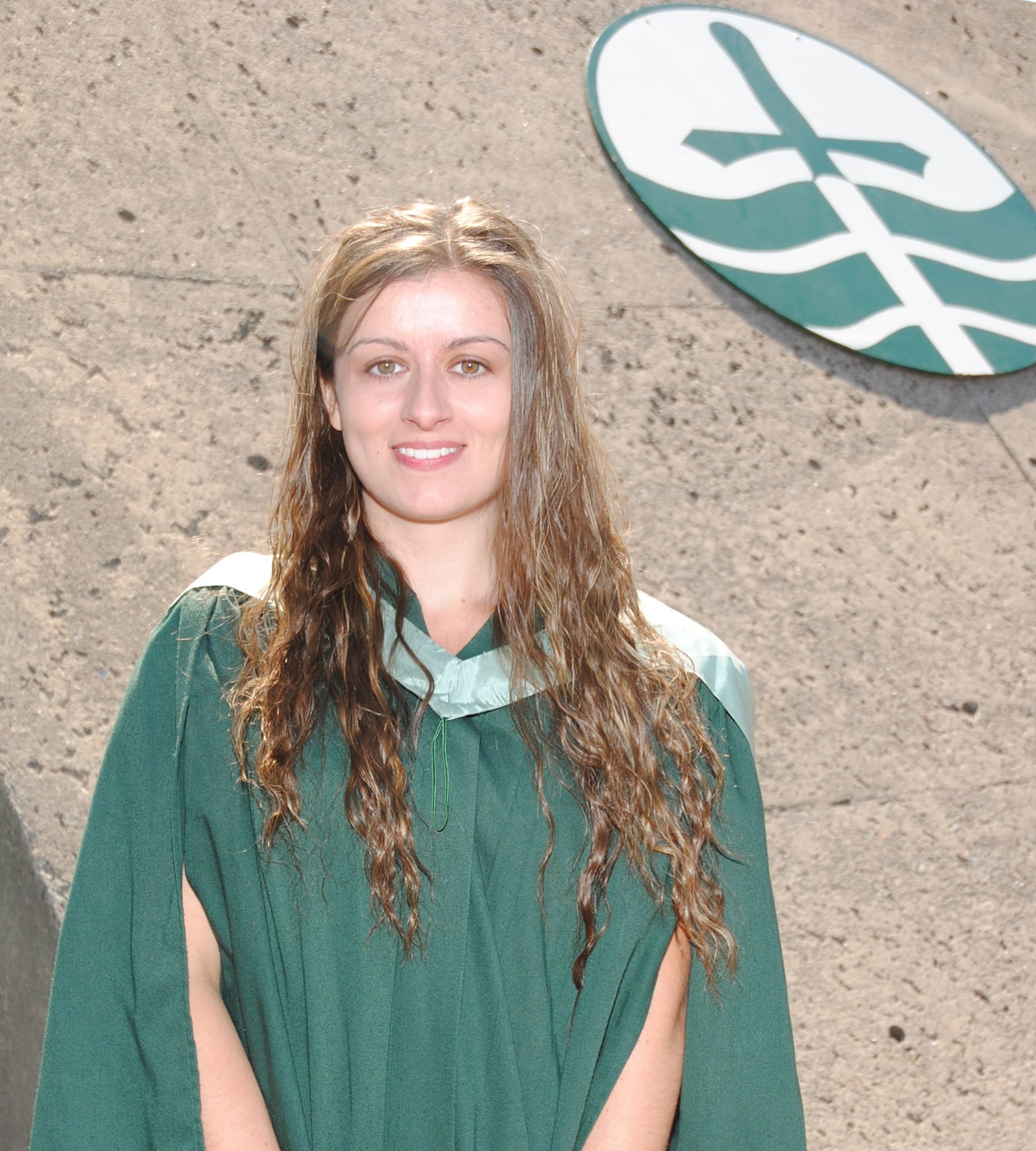 grad student Lindsay Thackeray wearing graduation gown smiling at camera with Trent emblem in background