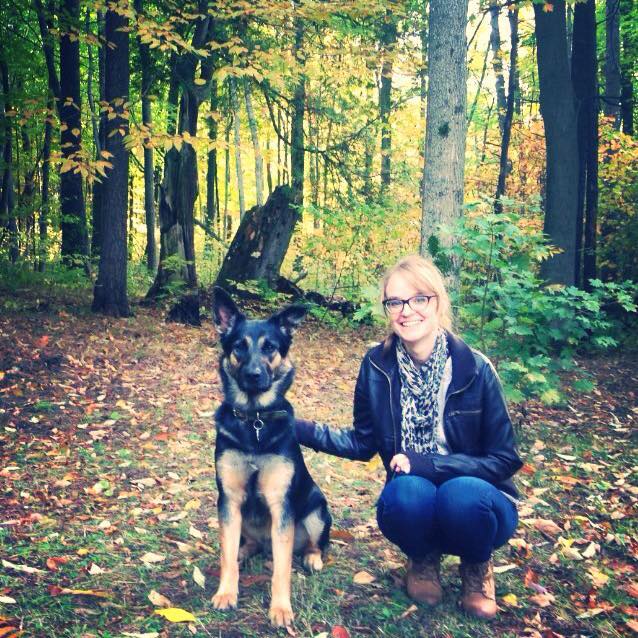 grad student Samatha Cunningham kneeling in forest with her dog smiling at camera