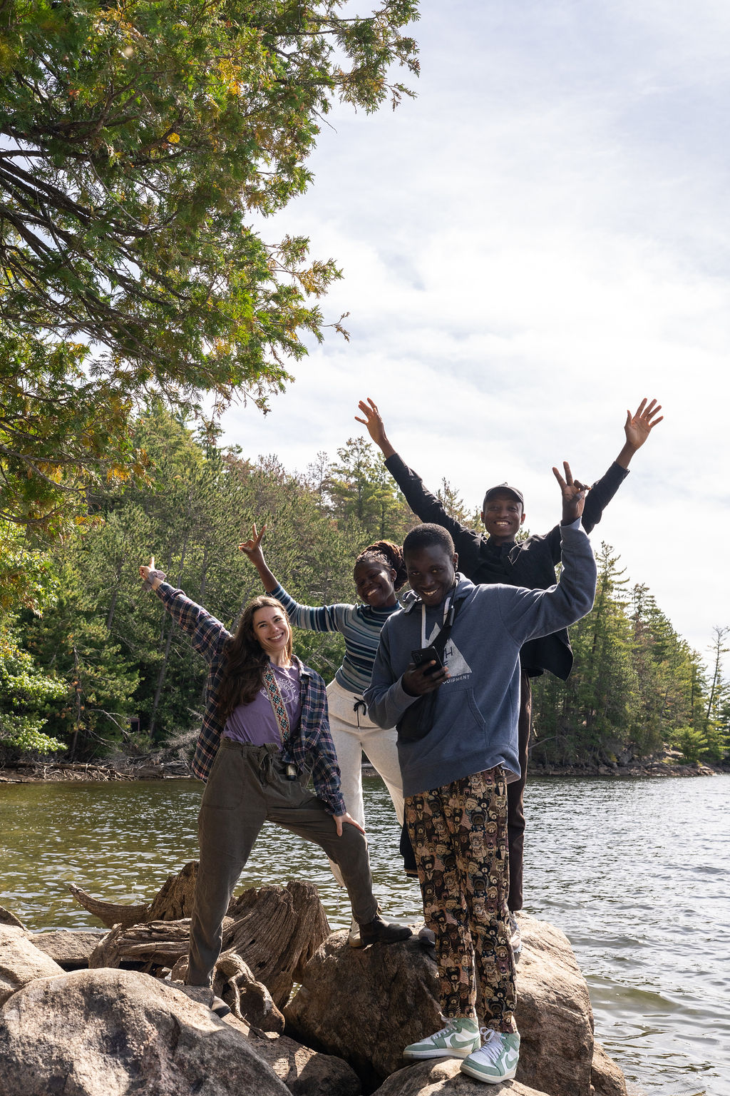 4 students standing at water with hands up in the air smiling
