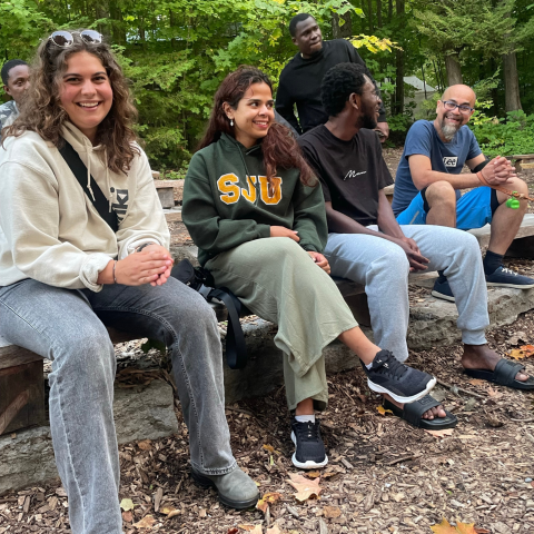 5 students sitting outside on a log