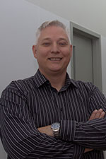 Man with short hair in striped dress shirt standing in Trent's chemical science building and smiling at the camera.