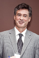 Man in suit and tie against a burgundy wall smiling at the camera 