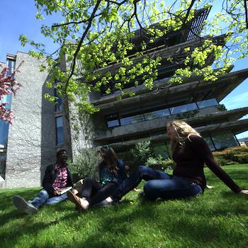 Three students sitting outside on the grass in front of Bata Library smiling