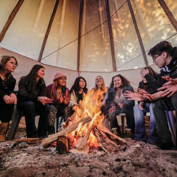 students sitting around a fire in a tipi