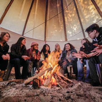 People sitting around a fire in a tipi