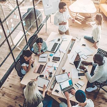 Overhead photo of people working collaboratively at a table with books and computers scattered over