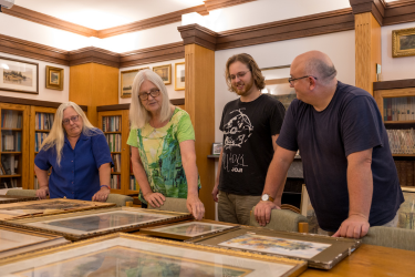 People standing at a table looking at old documents in picture frames