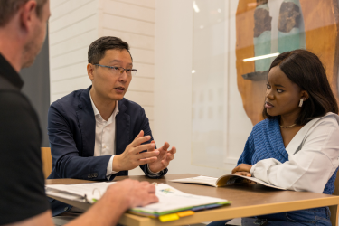 A professor and two students sitting at a table being taught