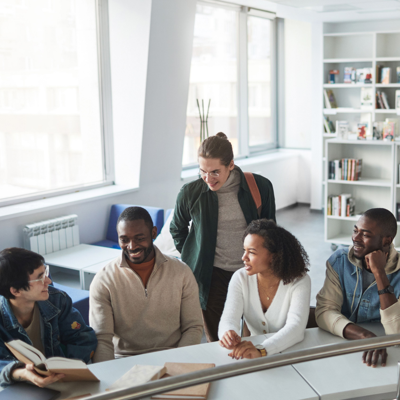 five people sitting and standing near a desk talking