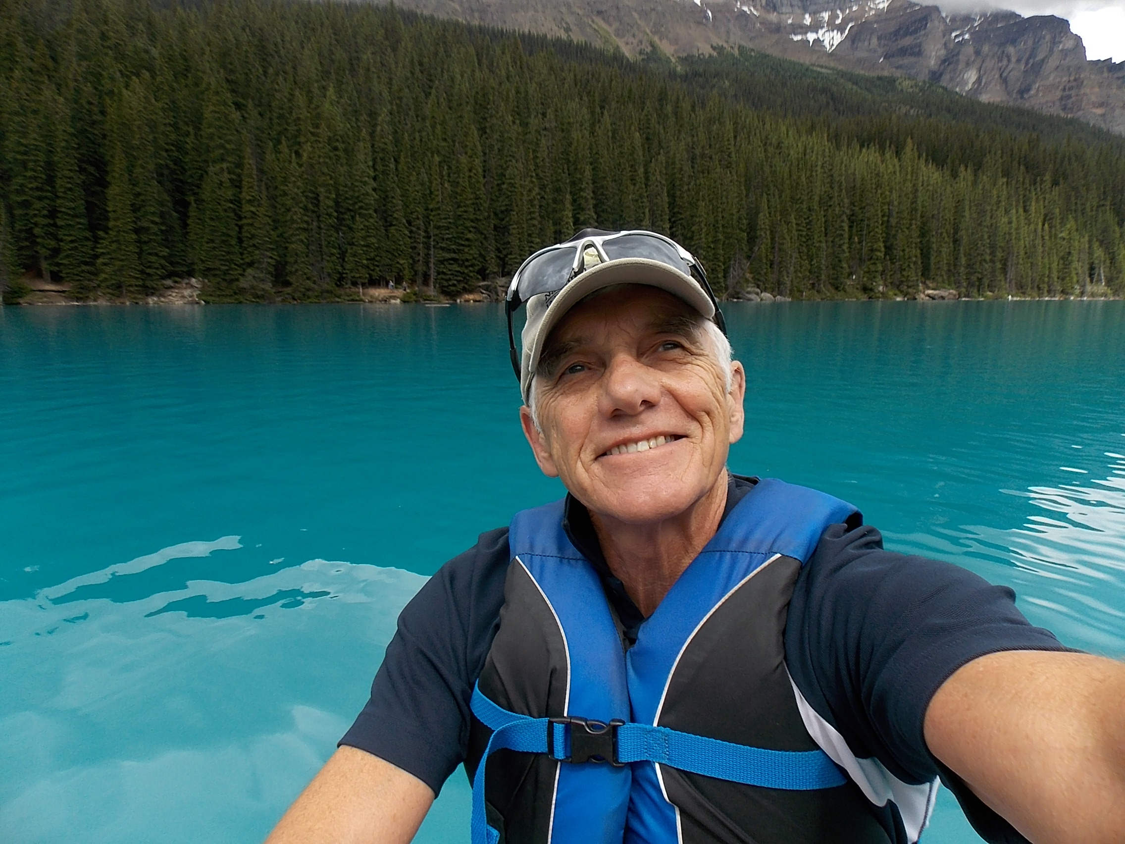 Dr. Alan Wright taking a selfie of a blue lake and a forest-lined shore from his canoe.