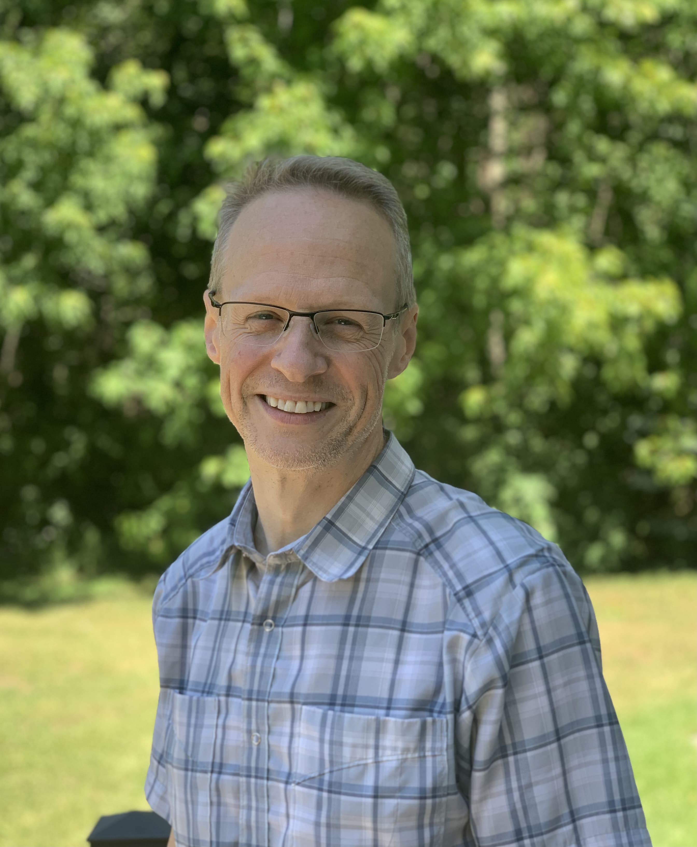 Chris, smiling, standing in front of trees