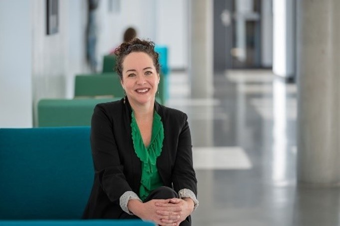 "Melissa Hill seated in a lit hallway"